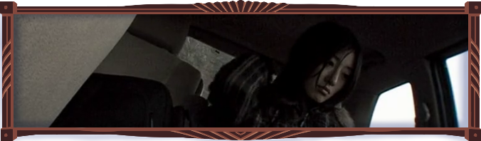 Still from the film. Marika Matsumoto looks sadly out the passenger window of a van window. The daylight outside is misty and very bright compared to the darkened, gloomy interior of the van. The colours are a uniform desaturated brown. The camera, sitting in the front passenger seat, is tiled to give the composition a feeling of unease.