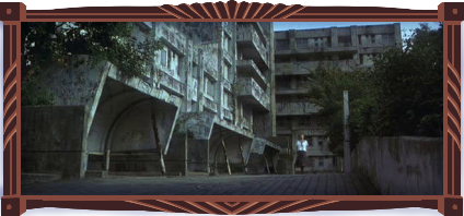A dilapidated postwar Japanese apartment complex: a brutalist structure made out of concrete, now covered in black grime and moss, with trees outgrowing the planters. A lone schoolgirl walks outside the building. The sky is bright. It’s eerie, but bright.