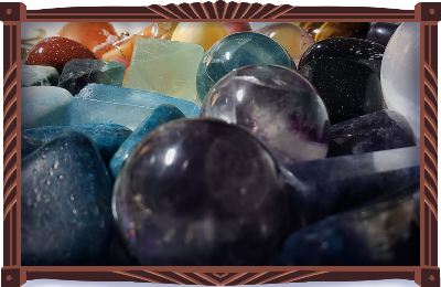 A bright assortment of tumbled, spherical, and obelisk stones, all sorted by color, arranged in a vintage Japanese porcelain bowl with gold floral trim and embellishments. Numerous specimens of fluorite with blue. Blue apatite, blue goldstone, a shining selenite sphere, blued aqua aura quartz. In the back, amazonite, red goldstone, carnelian, fire agate, mookaite jasper…